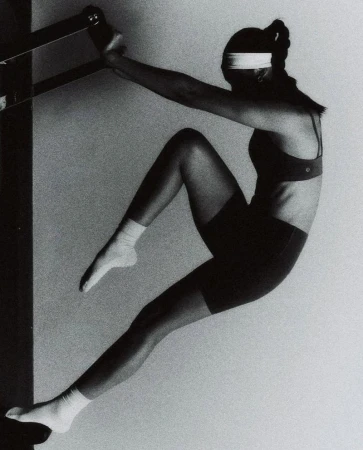 Athletic woman in sports bra and shorts doing inverted Pilates exercise using a wall-mounted ladder barre for core strength and flexibility.