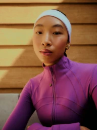 Maureen Tang wearing a purple zip-up jacket and light headband posing in front of a wooden panel wall.