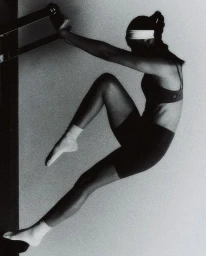 Monochrome shot of a woman in a sports bra, biker shorts, white headband, and socks gripping a frame in an athletic pose.