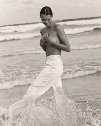 Woman wearing white trousers wading through ocean surf at the beach