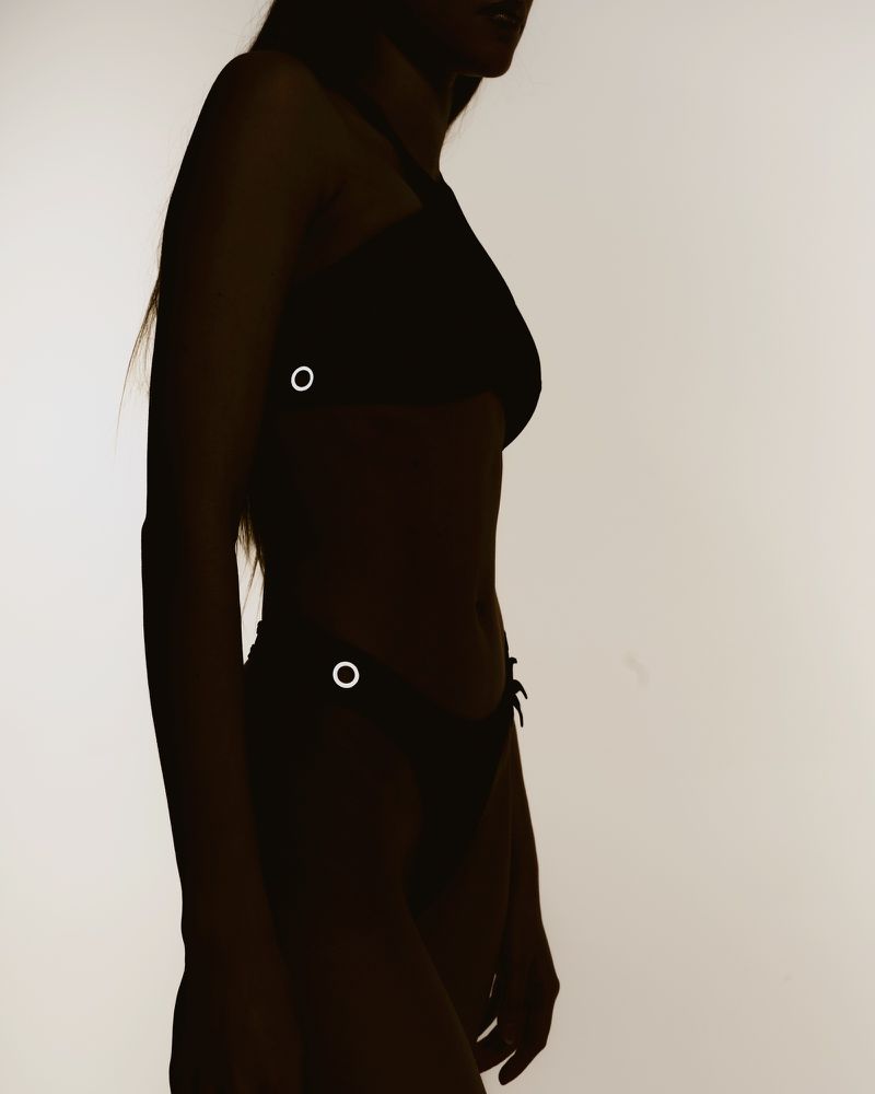 Silhouette of an adult woman in a two-piece swimsuit against a light background. Side view showcases the contours of her figure.