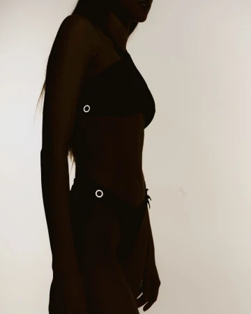 Silhouette of an adult woman in a two-piece swimsuit against a light background. Side view showcases the contours of her figure.