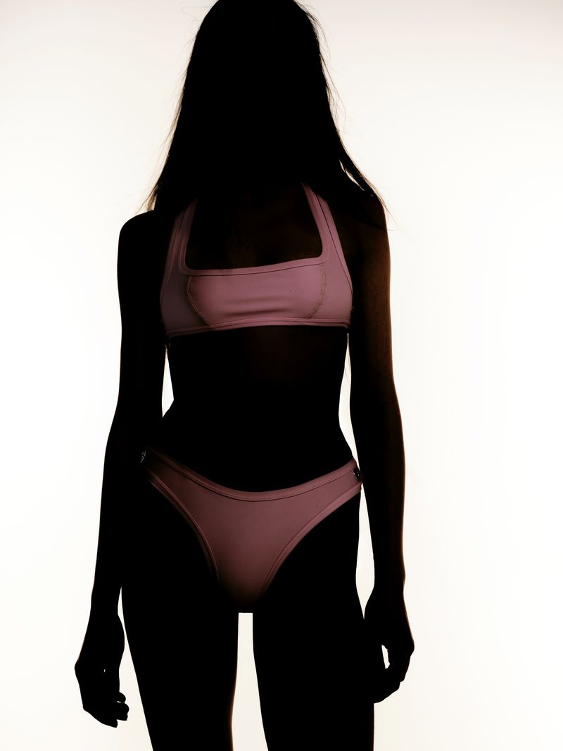 Silhouette of a woman wearing a pink bikini against a bright white background. Dark figure highlights the swimwear's shape and design.