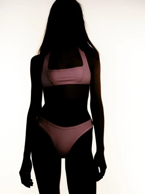 Silhouette of a woman wearing a pink bikini against a bright white background. Dark figure highlights the swimwear's shape and design.