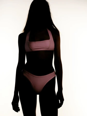 Silhouette of a woman wearing a pink bikini against a bright white background. Dark figure highlights the swimwear's shape and design.