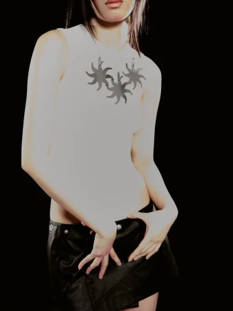 Cropped view of a model wearing a white graphic sleeveless top with sun motifs and a black low-rise mini skirt against a black background.