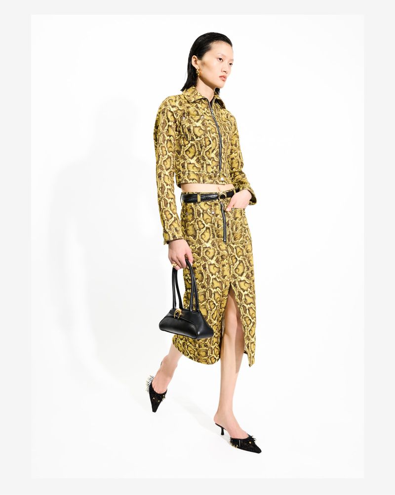 Model Yilan Hua posing in a yellow snakeskin cropped jacket and matching skirt holding a black handbag against a white background.