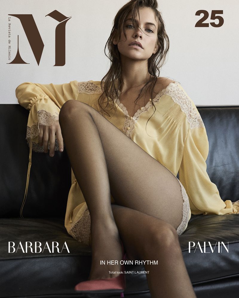Barbara Palvin on a magazine cover in a yellow lace-trimmed top and black tights, poses on a black couch against a white background.