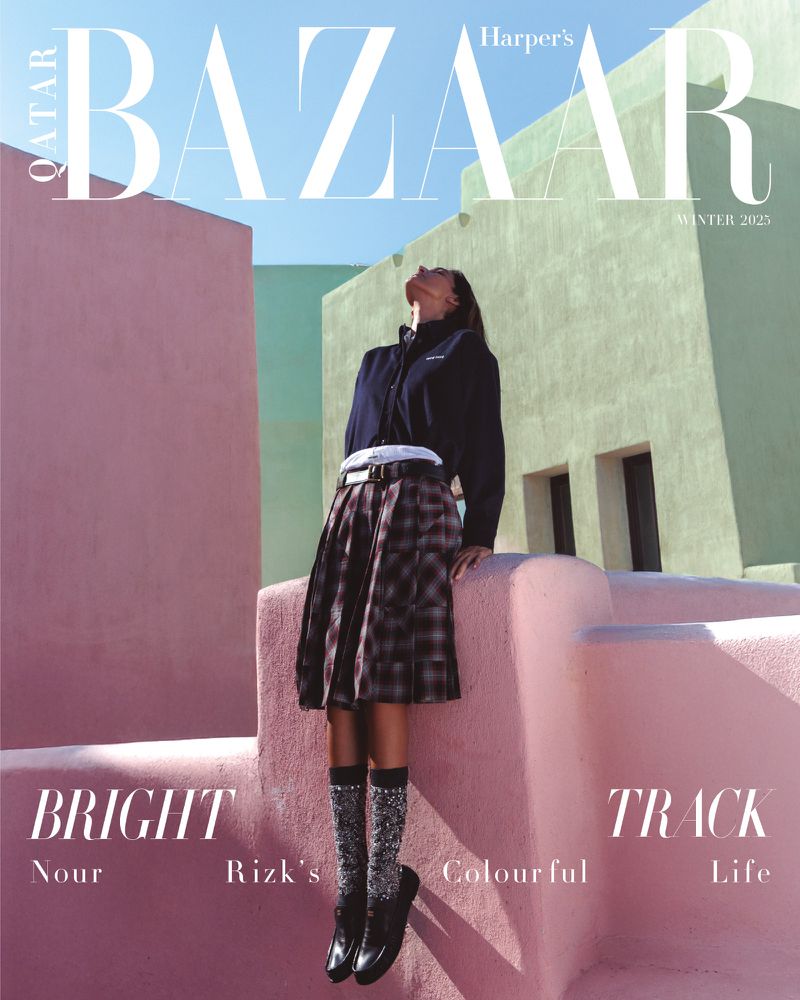 Harper's Bazaar cover featuring a fashionable woman in a pleated skirt, platform shoes, and a dark jacket set against colorful buildings.