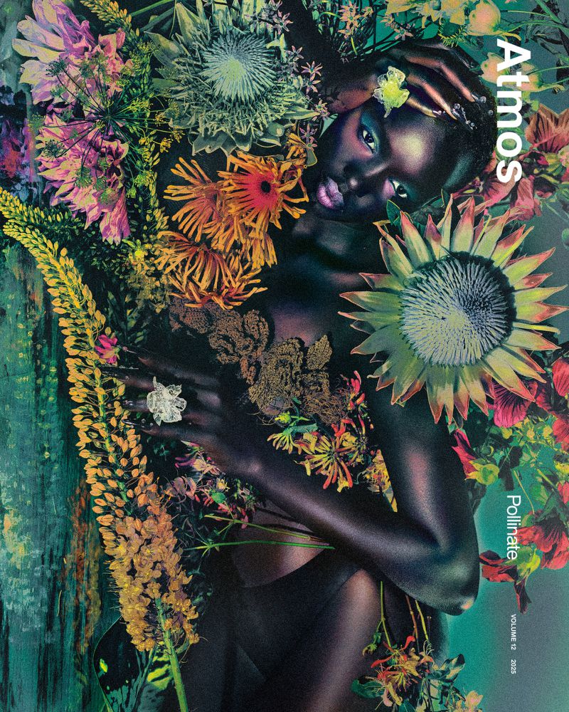 Dark-skinned woman with floral decorations, editorial style. Close-up of model surrounded by colorful flowers and greenery in a studio shot.