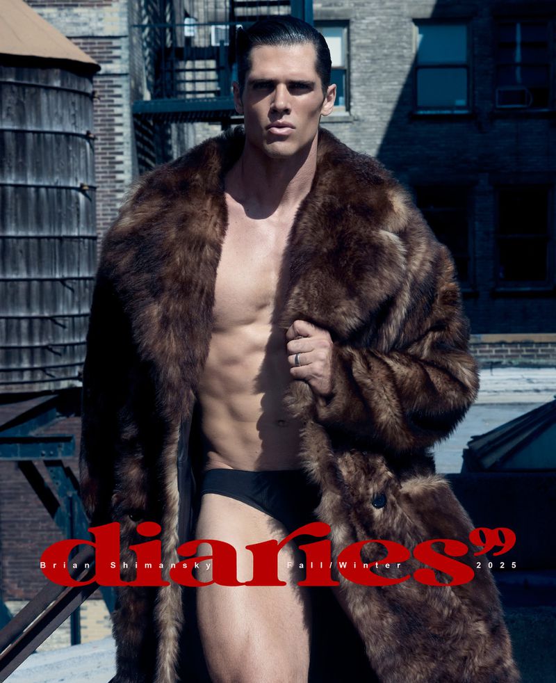 Male model poses shirtless in a brown fur coat against a cityscape backdrop, featuring visible abs and dark hair slicked back.