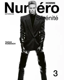 Model Taras Romanov poses on a white studio background wearing a tailored blazer, black leather gloves, and thigh-high boots.