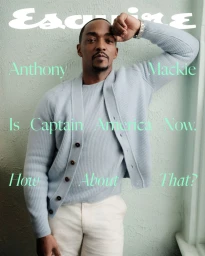 Anthony Mackie wearing a pale blue knit cardigan and white trousers leaning against a textured wall for Esquire U.S.