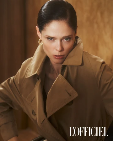 Stylish portrait of a woman in a tan trench coat with wet hair, set against a textured backdrop, captured in a studio setting.