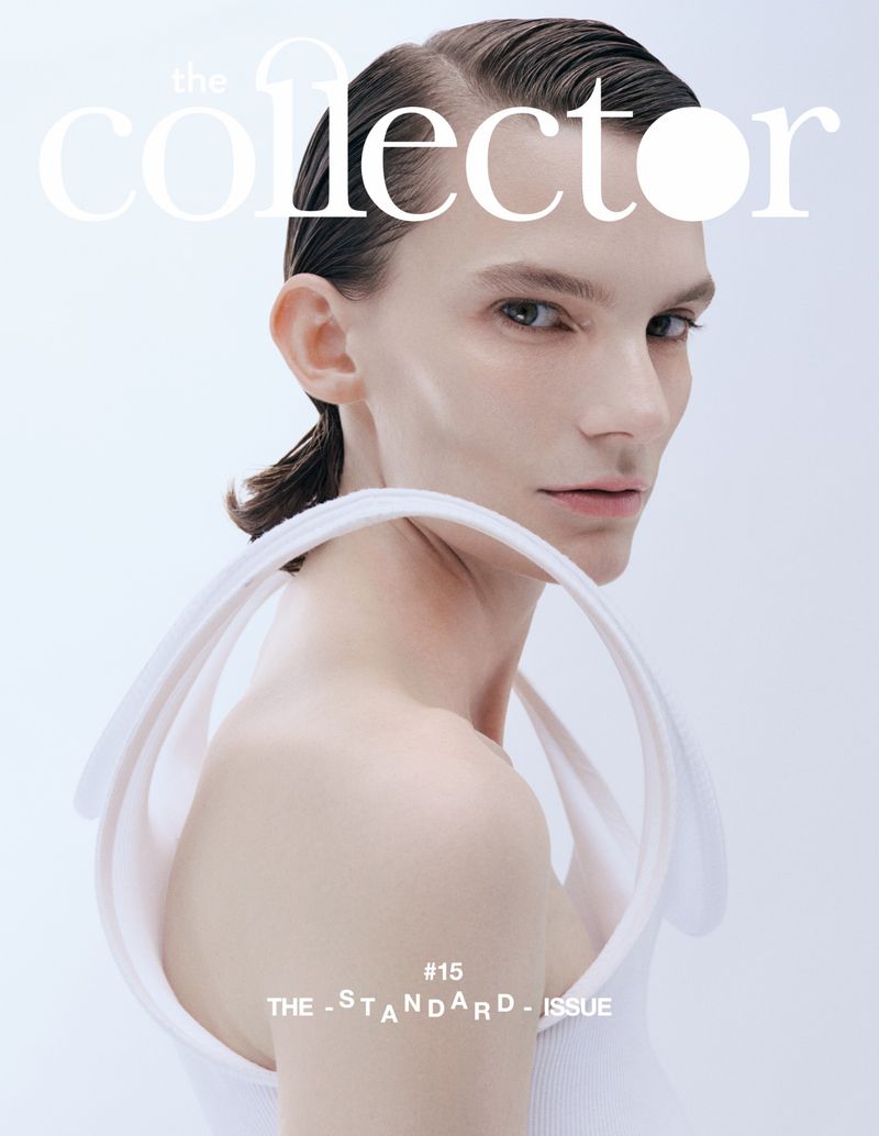 Magazine cover featuring a model with slicked-back hair wearing a white top with circular straps, against a light grey background.