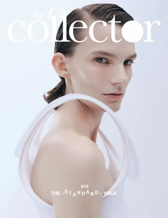 Magazine cover featuring a model with slicked-back hair wearing a white top with circular straps, against a light grey background.