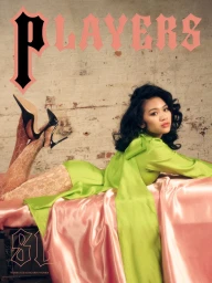 Suni Lee wearing a lime green top and patterned tights reclining on pink satin against an exposed brick wall for Players magazine.