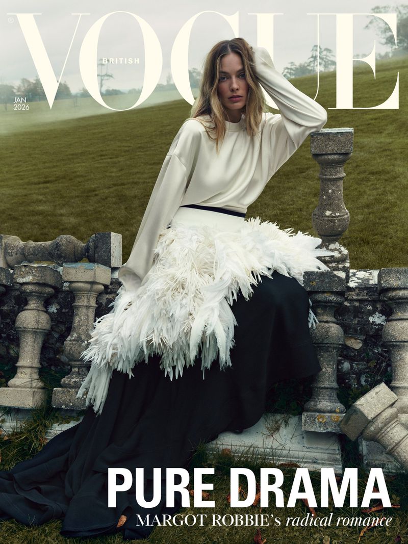 Vogue cover featuring Margot Robbie in a white top and black skirt with white feather accents, posing on a stone structure.
