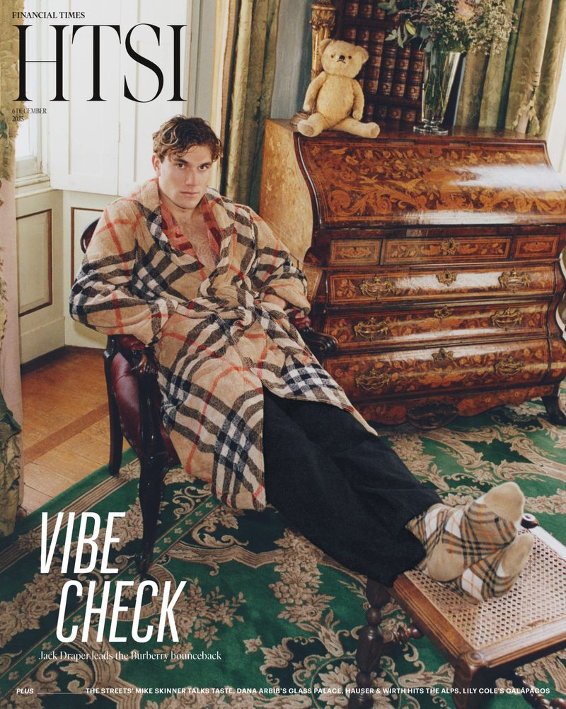 Magazine cover featuring an adult man in a Burberry robe and socks sitting in a room with a teddy bear on top of a desk.