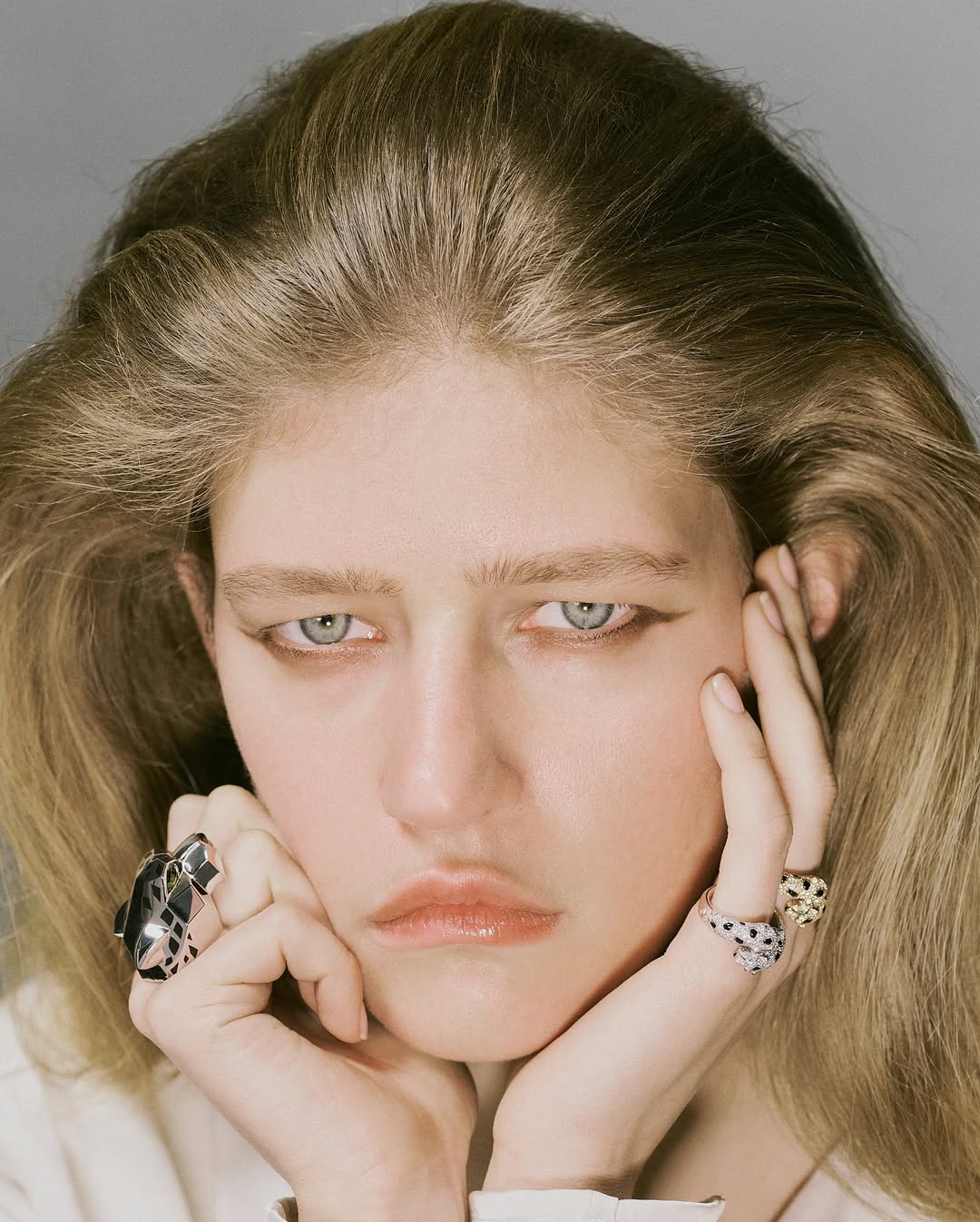 Close-up portrait of a young adult woman with blonde hair and light eyes, wearing rings and facing the camera.