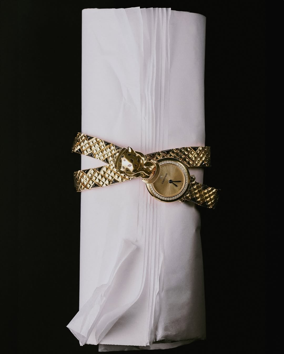 Elegant gold wristwatch with panther detail nestled in soft white tissue paper against a dark background, showcasing luxury jewelry.