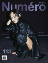Woman with long dark hair wearing a black leather coat and tall boots crouching against a dark purple background.