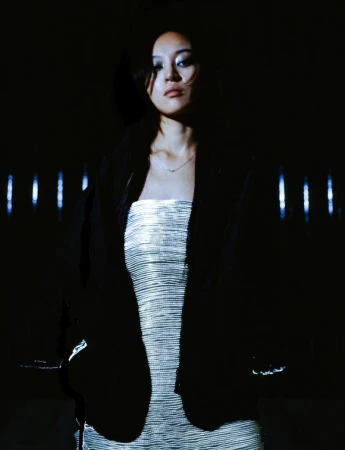 Pan Daijing wearing a strapless metallic silver ribbed dress and an open black jacket against a dark background with vertical lights.