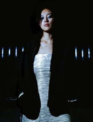 Pan Daijing wearing a strapless metallic silver ribbed dress and an open black jacket against a dark background with vertical lights.