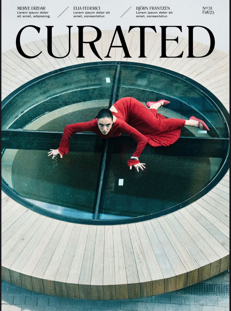 Magazine cover featuring a woman in a red dress in a crawling pose, set against a round glass architectural feature.
