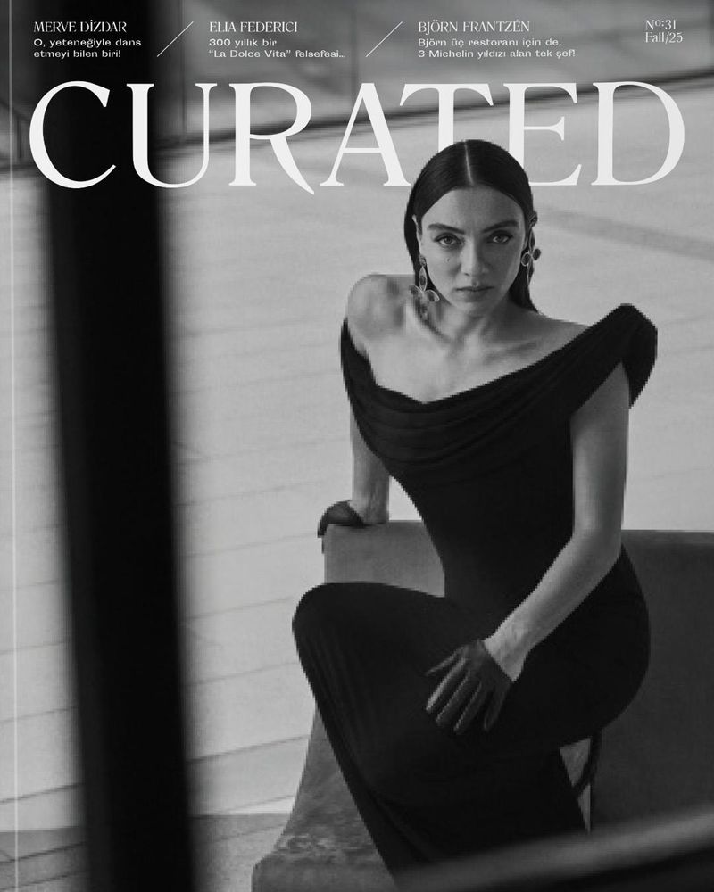 A monochrome fashion magazine cover with a woman in a black dress, striking a seated pose, featuring a curated layout and bold typography.