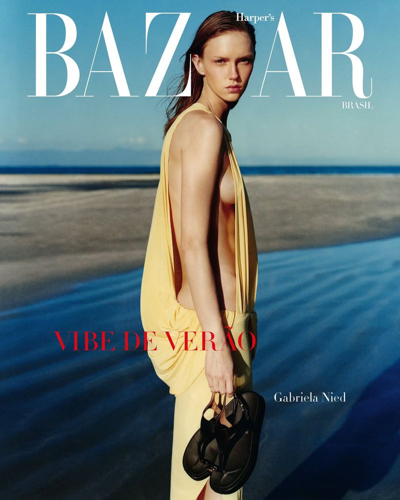 Harper's Bazaar cover featuring a woman in a yellow dress standing on a sandy beach with water, blue sky, and holding black sandals.