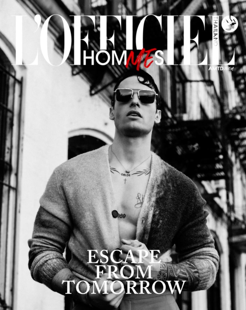 Black and white fashion magazine cover featuring a shirtless male model in a cardigan against a blurred urban backdrop.