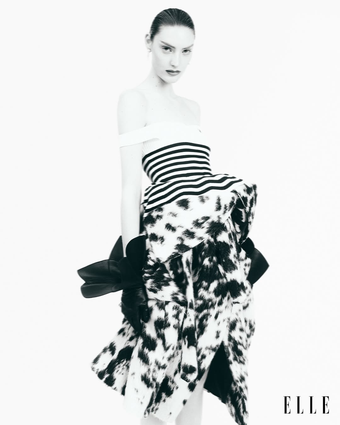 A fashion shot of a woman in a black and white striped top and a dalmatian print skirt posing in a photo studio with the Elle logo.