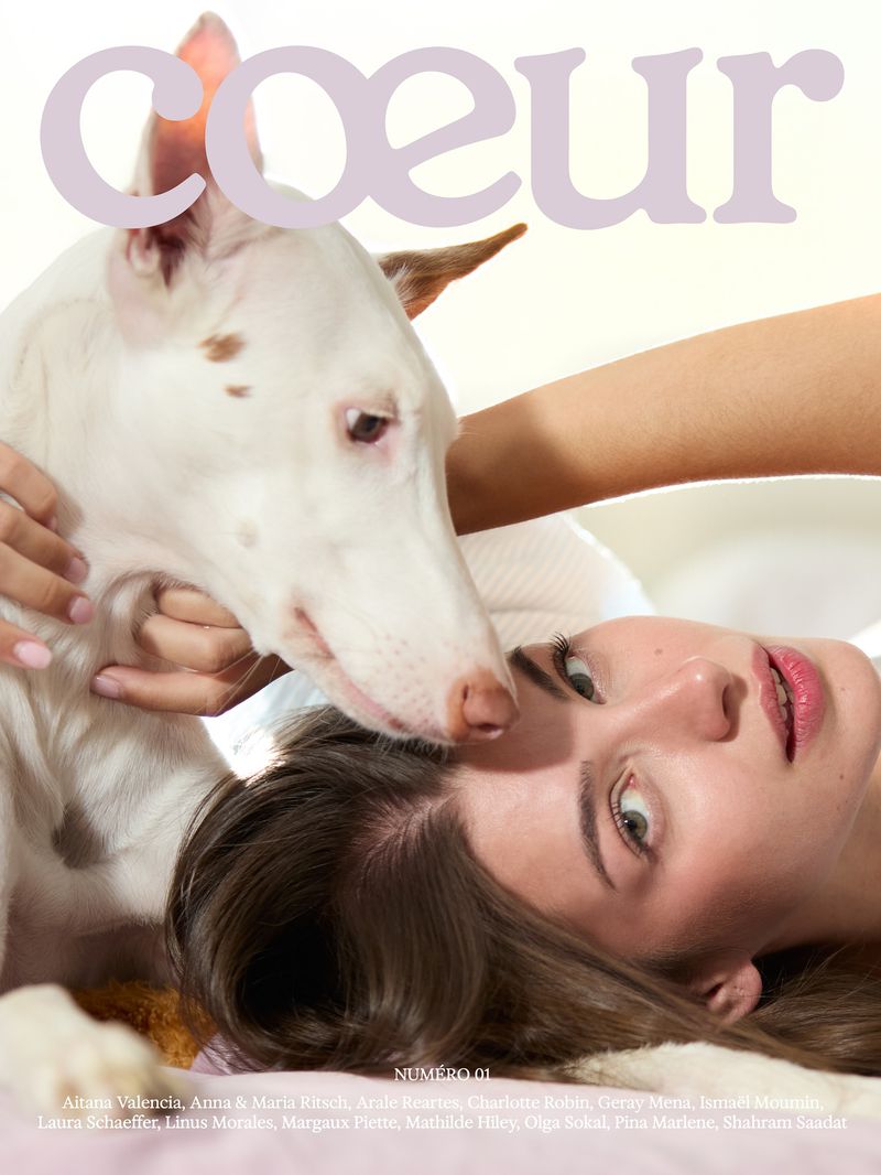 Magazine cover features a woman lying down with a white dog, the masthead reads Coeur, eye-level angle, soft focus, intimate moment.
