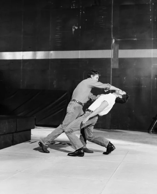 Two adult males are stage fighting in a studio. One male is choking the other in a black and white, medium shot, eye-level photo.