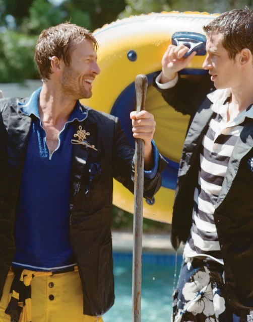 Two adult men are standing outside near a pool, one holding a pole, with an inflatable float in the background, captured at eye-level.