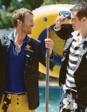 Two adult men are standing outside near a pool, one holding a pole, with an inflatable float in the background, captured at eye-level.