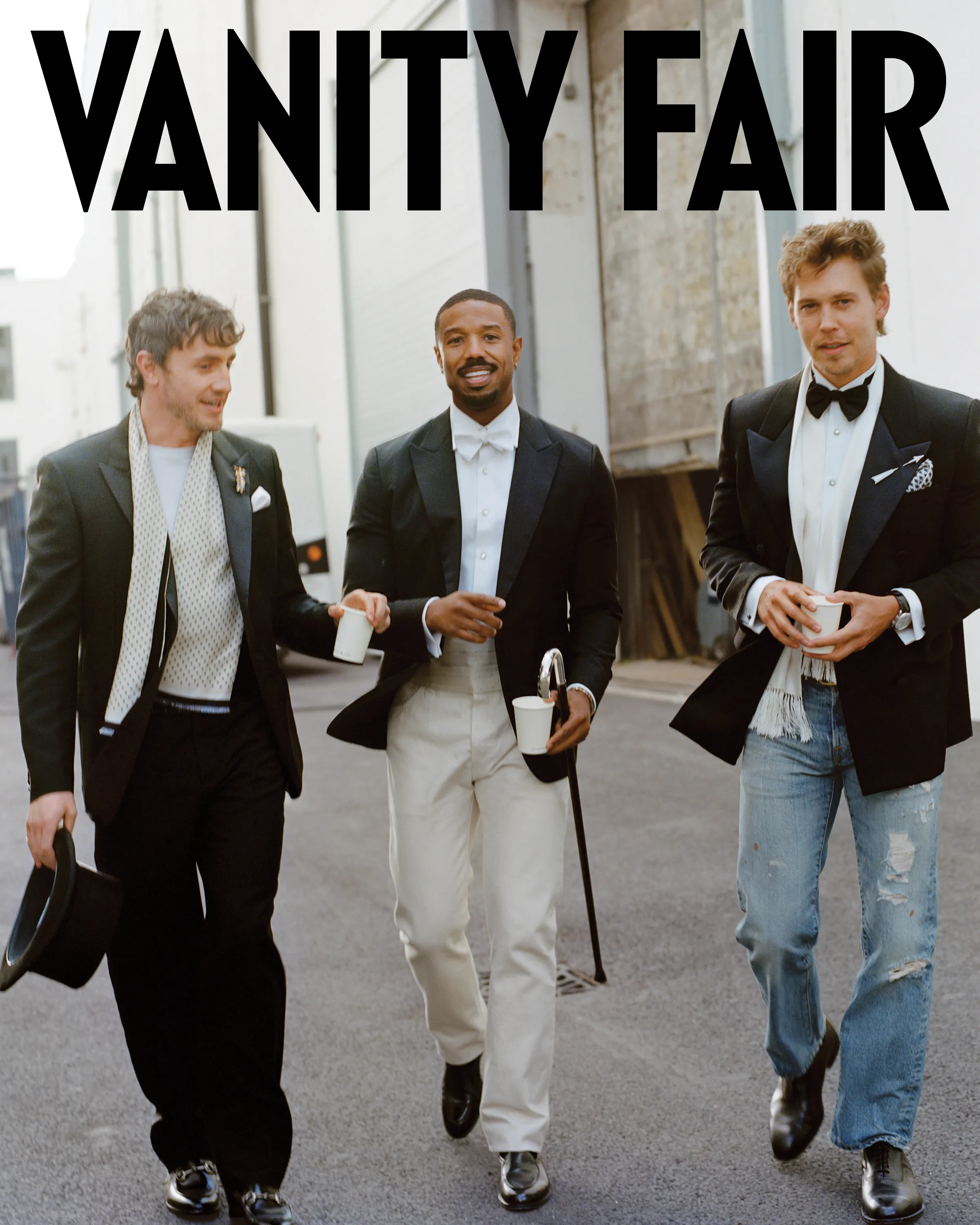 Three men walking outside, dressed in tuxedos and holding cups, photographed for Vanity Fair with the magazine's logo visible.
