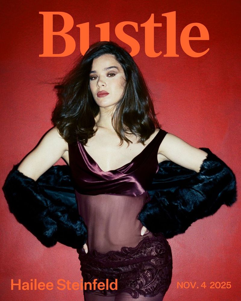 Bustle magazine cover featuring Hailee Steinfeld in a velvet and lace dress with fur stole against a red backdrop and orange text.