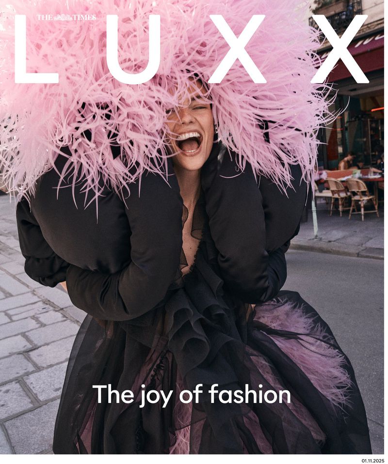Magazine cover featuring a smiling woman with a large pink feathered headpiece, wearing a black dress, on a Parisian street.