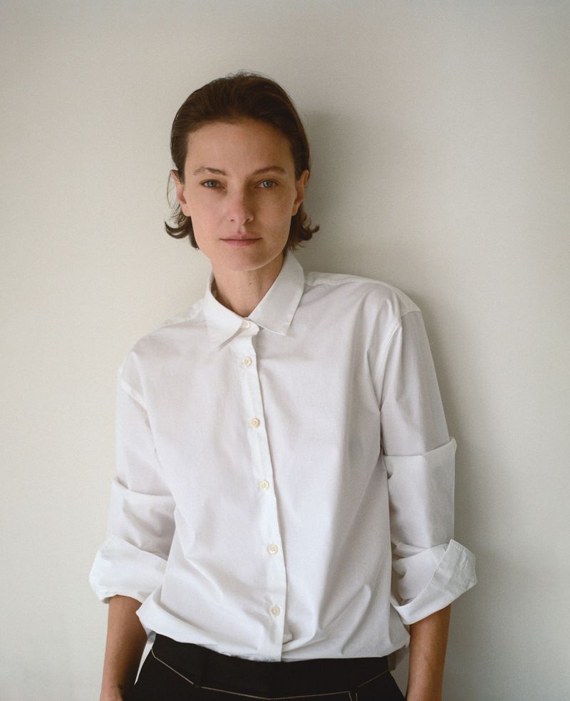 Model Tanya Ruban wearing a crisp white button-down collared shirt with rolled cuffs against a neutral pale wall.