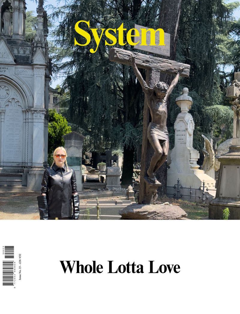 Fashion magazine cover features a woman in a black leather outfit posing in a cemetery with a crucifix and tombstones.