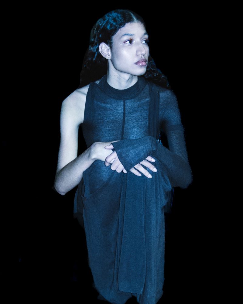 Young adult poses in a dark fashion portrait wearing a sheer black top with interesting sleeves, looking left in a dramatic fashion photograph.