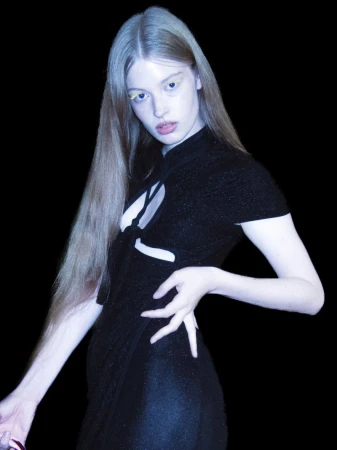 Model wearing a black cutout dress with light yellow eyeshadow posing against a solid black background.