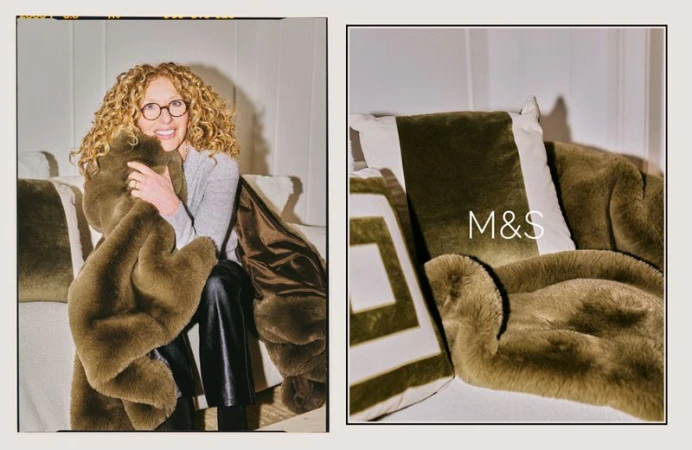 Indoor shot of an adult female with curly hair, glasses, grey shirt and black pants, sitting on a white couch holding a brown blanket.