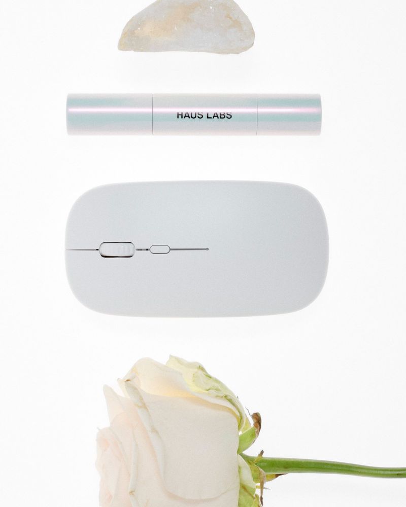 High-angle shot showcasing a computer mouse, flower, cosmetic product, and rock on a white surface, creating a minimalist aesthetic.