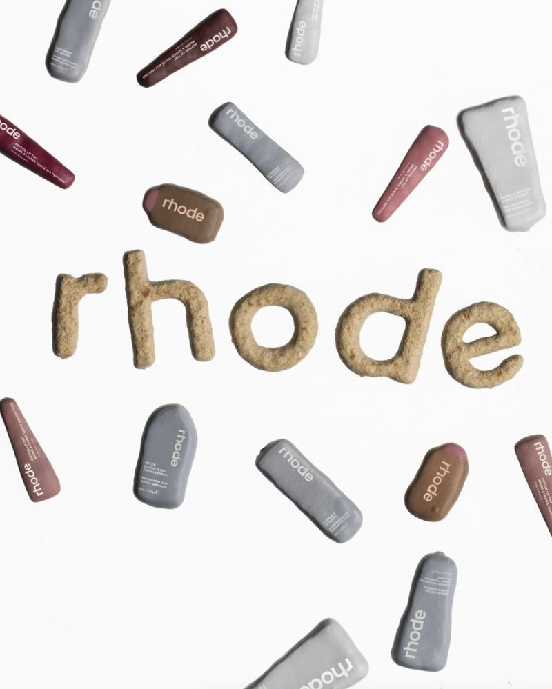 Floating arrangement featuring Rhode skincare product containers and the Rhode brand name spelled out, against a white backdrop.
