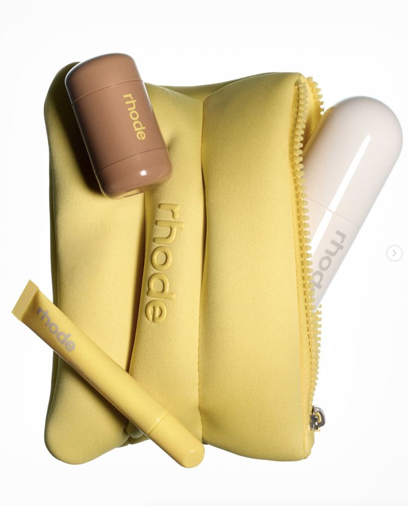 Cosmetic bag in lemon yellow with skincare products from Rhode including a balm, moisturizer, and serum. Beauty product flat lay.