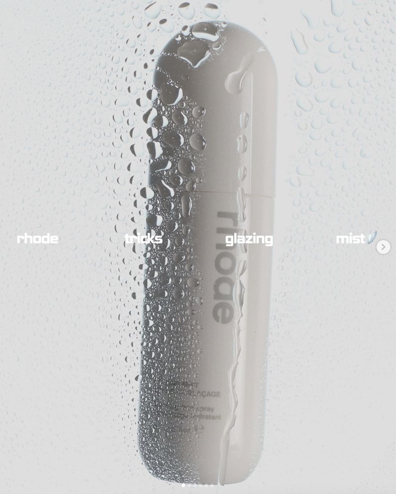 Close-up studio shot of a white Rhode skincare bottle covered in water droplets against a white background with visible brand text.