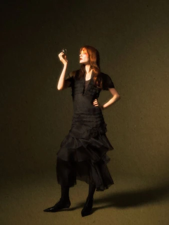Model Sabi Khazgaleeva in a tiered black midi dress holding a small translucent sphere in a dark studio setting.